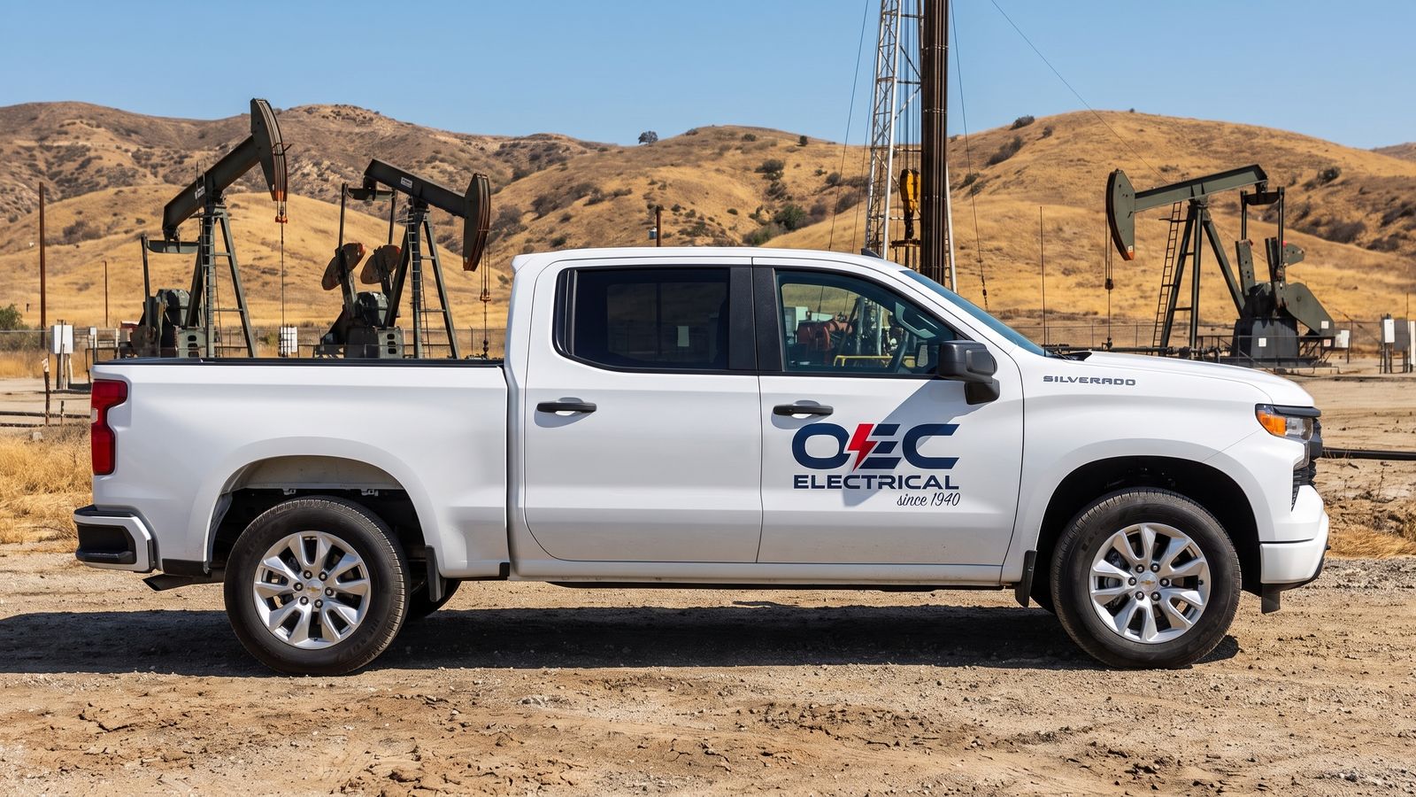 White OEC Electrical Chevrolet Silverado service truck at a Southern California oil field with pump jacks and a derrick
